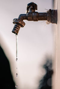 Close-up of water falling from faucet against sky