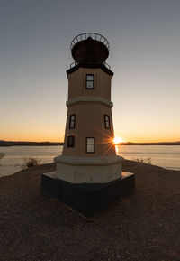 Lighthouse by sea against sky during sunset