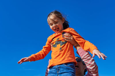 Pretty girl being held up in the air by mom against a blue sky