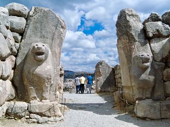 People on rock against cloudy sky