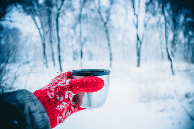 Girl with long hair in red gloves with ornament holding tourist from thermos cup. during snowfall. 