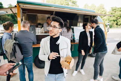 Male customer with box talking to friend while standing against food truck