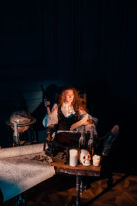 Young woman sitting on table in illuminated room