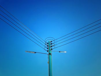 Low angle view of electricity pylon against clear blue sky