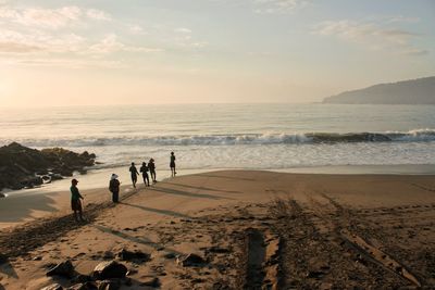 People walking on beach against sky during sunset