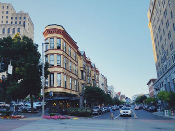 Cars on city street by buildings against clear sky