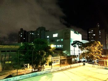 Illuminated street by buildings against sky at night