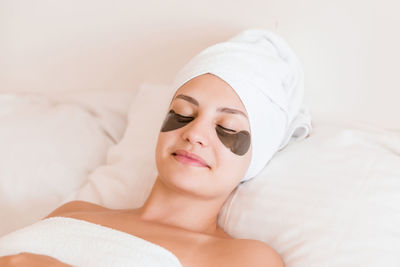 Smiling young woman with under eye patches lying on bed at spa