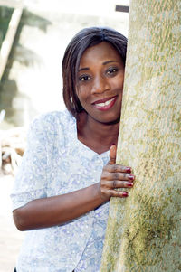 Smiling young woman leaning against a tree, looking at the camera