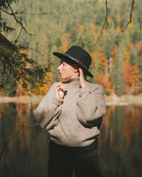 Man wearing hat standing by lake in forest during autumn