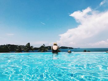 Rear view of woman with daughter swimming in pool by sea against cloudy sky