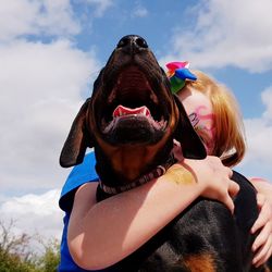 Close-up of girl embracing dog against sky