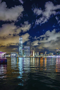 Illuminated city by sea against sky at night