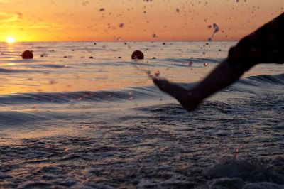 Low section of person splashing water at beach during sunset