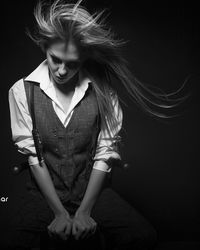 Young female model sitting on chair against black background