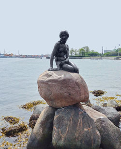 Statue on rock by sea against clear sky