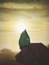 Person holding umbrella against sky during sunset