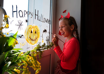 Child painting pumpkin window preparing celebrate halloween kid draws decorates room with paper bats