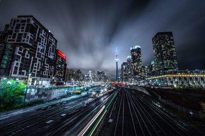 Illuminated railroad tracks amidst buildings in city at night