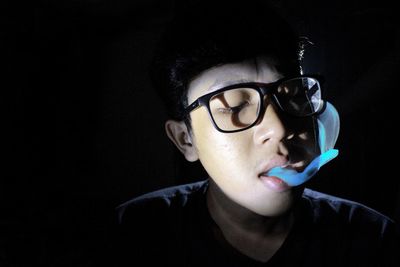 Close-up of young man exhaling smoke against black background