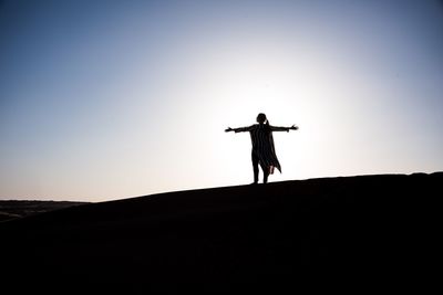 Silhouette man with arms outstretched standing on land