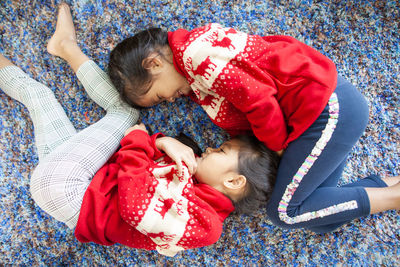 High angle view of smiling sisters lying on rug at home