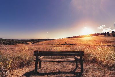 Empty bench on field against sky during sunset