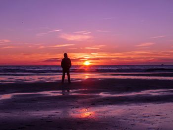 Silhouette man standing on beach against sky during sunset