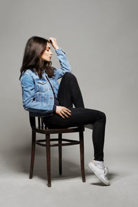 Woman sitting on chair against wall