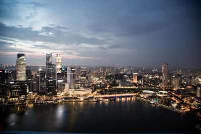 Illuminated buildings by river against sky in city