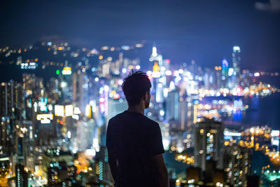 Rear view of man looking at illuminated city buildings at night