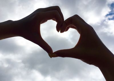Cropped image of hands making heart shape against cloudy sky