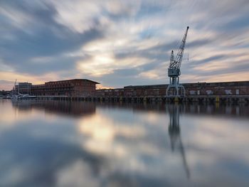 Sailboats in river by buildings against sky during sunset