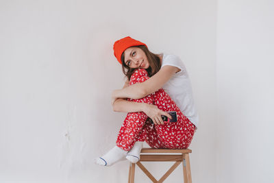 Smiling funny girl in a red hat and christmas pajamas sitting in bed with white sheets. 