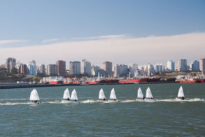 Sailboats in sea by buildings against sky