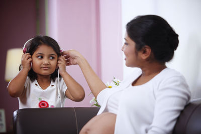 Girl listening music with pregnant mother while sitting on sofa at home