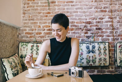 Young woman smiling while standing against brick wall