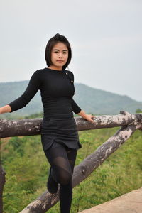Portrait of young woman standing by railing on observation point against sky