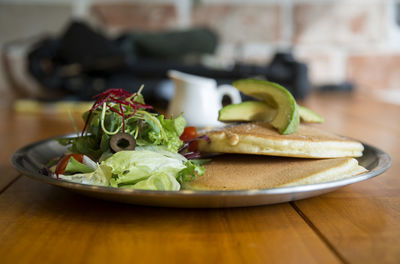 Close-up of pancakes with salad served in plate on wooden table