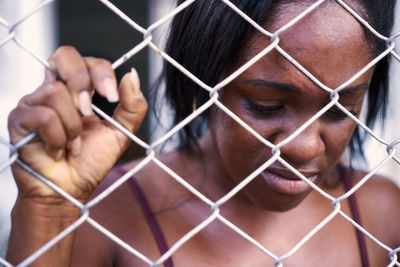 Shirtless sad woman holding chainlink fence