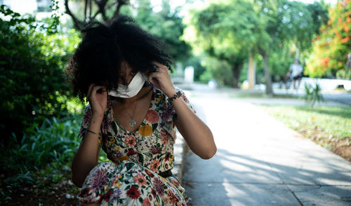 Young woman with a mask standing by tree against plants