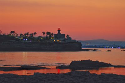 Lighthouse by sea against sky during sunset