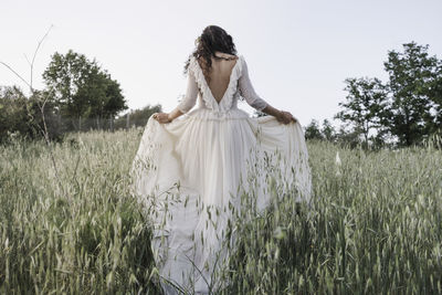 Rear view woman wearing dress standing amidst plants on land