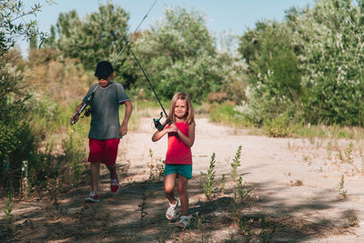 Full length of siblings with fishing rods walking on field