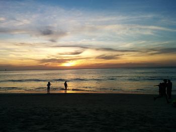 Silhouette people standing on beach against sky during sunset