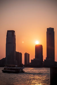 Modern buildings by sea against sky during sunset