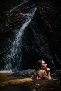 Side view of woman lying in river against waterfall
