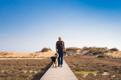 Rear view of man walking with dog against sky