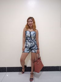 Full length portrait of young woman standing against wall