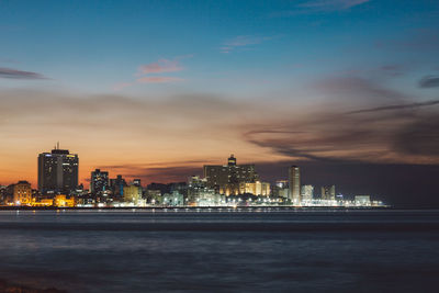 Illuminated city by sea against sky at night